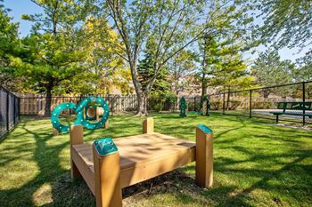 A wooden bench with a green trash can next to it in a park.